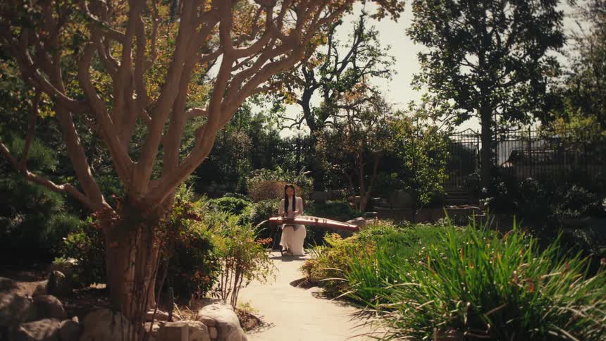 A woman is playing a traditional chinese string instrument in a sunlit lush garden
