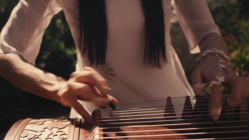 A woman playing a guzheng a traditional chinese plucked string instrument with 21 strings her fingers delicately plucking the strings as she sits in a white dress