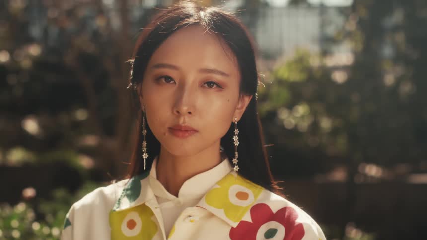 Woman wears long dangling earrings containing flowers and a shirt with similar flowers on a sunny day