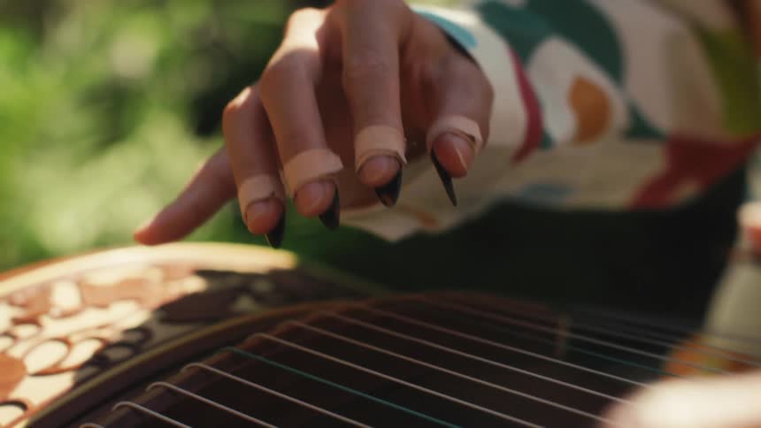A woman with a floral pattern adorning her shirt gracefully plays the guzheng a traditional chinese plucked string instrument