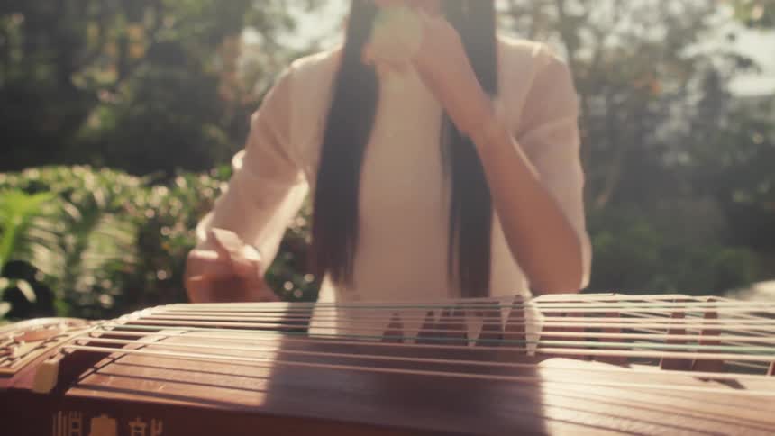 A woman dressed in traditional attire playing a guzheng a chinese stringed instrument outdoors in a serene sunlit garden
