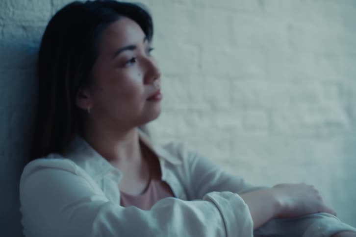 Woman with a white shirt and crimson pants leans against the white brick wall