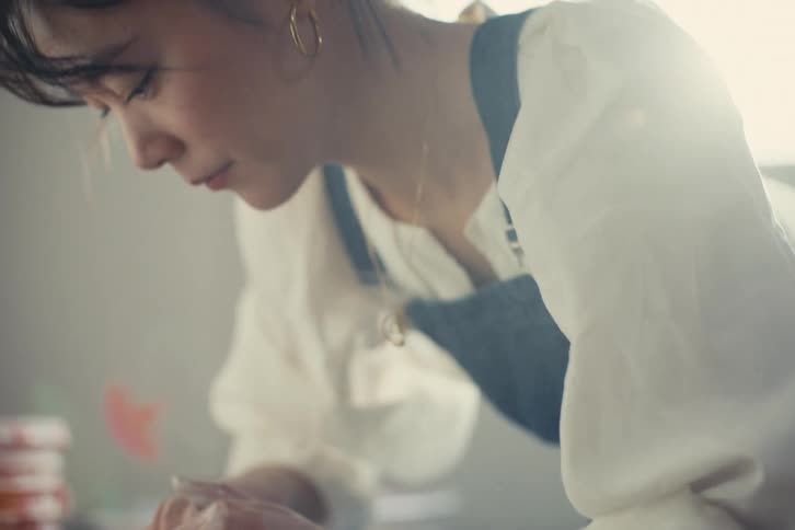 Woman with hoop earrings a white shirt a blue apron and a necklace carefully shaping a wet clay pot on a spinning wheel