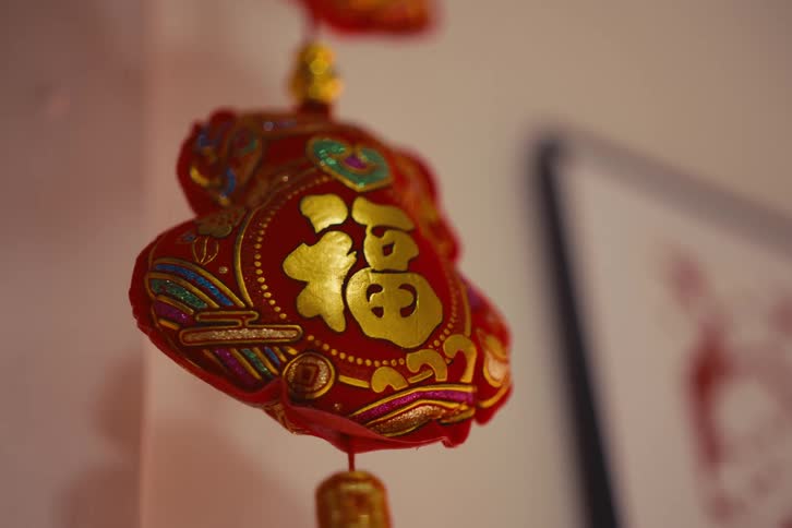A red chinese lantern with gold lettering and intricate patterns hanging from a ceiling