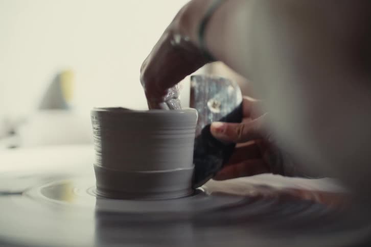 A potters hands skillfully shaping a wet clay pot on a spinning wheel their fingers delicately smoothing the surface as it rotates creating a beautiful and symmetrical form