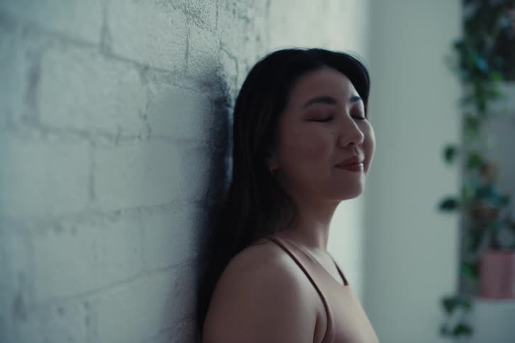 Woman in an indoor space leaning against the wall and smiling