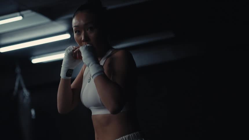 The woman in the white sports bra is boxing in front of punching bags