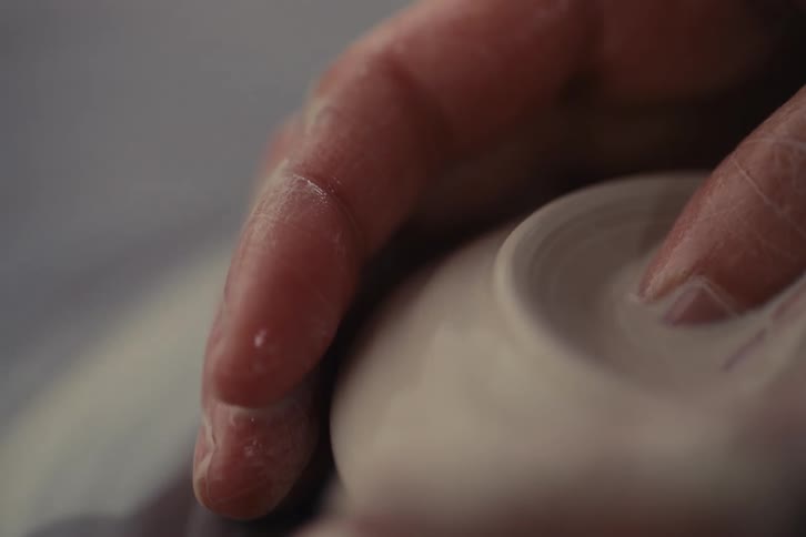 A womans hand shaping a small wet clay pot