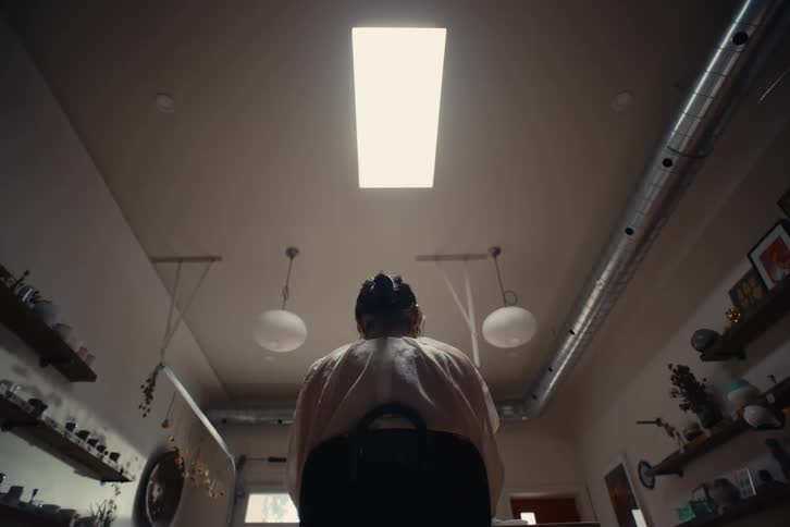Back view of a woman sitting on a chair in a room with shelves and objects