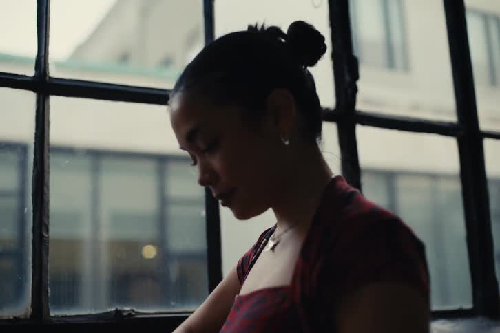 Woman in an indoor space looking down next to a window