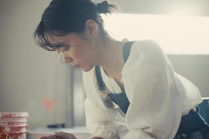 Woman with hands dirty with white clay holding a drum in an indoor space