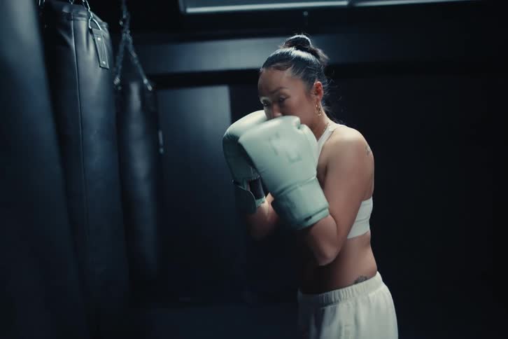 A woman wearing boxing gloves and a sports bra is practicing boxing in a dimly lit gym