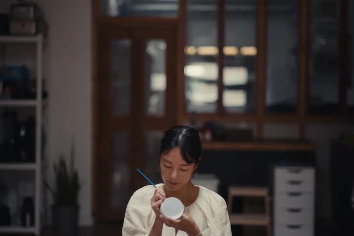 A woman is using a pen to write on a white mug
