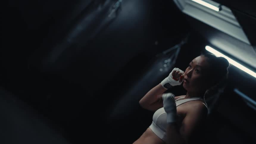 Female air boxing in a darkened gym near boxing bags