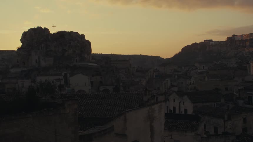 A dramatic sunset over a picturesque town nestled on a cliff with a prominent cross silhouetted against the fiery sky