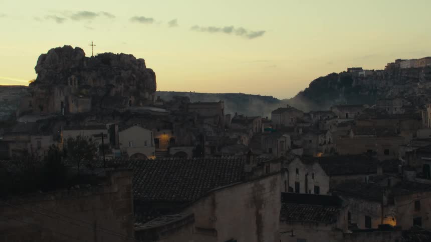 A picturesque view of an ancient town at dusk with a rocky hill topped by a cross