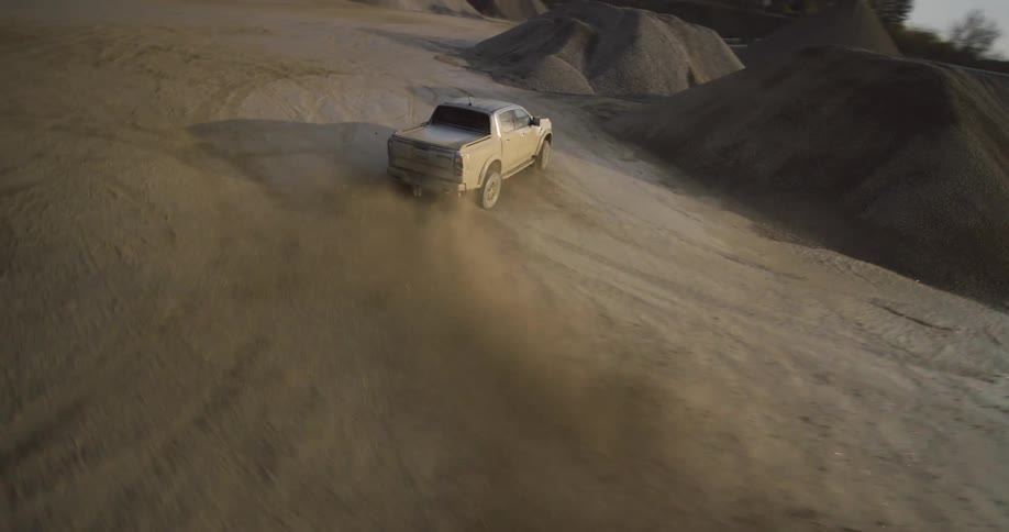 A pickup truck drives through a dirt and sand area kicking up dust