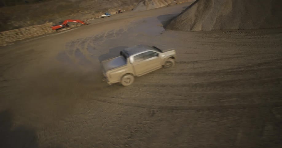 A silver pickup truck driving through a muddy construction site with machinery and piles of dirt in the background