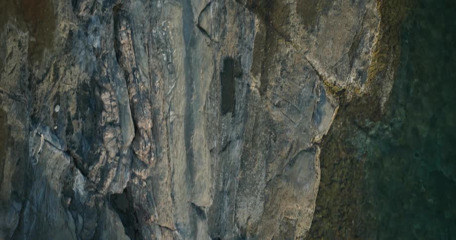A rocky cliff face with visible layers and cracks a thin yellow line running through the center meeting a dark rough sea