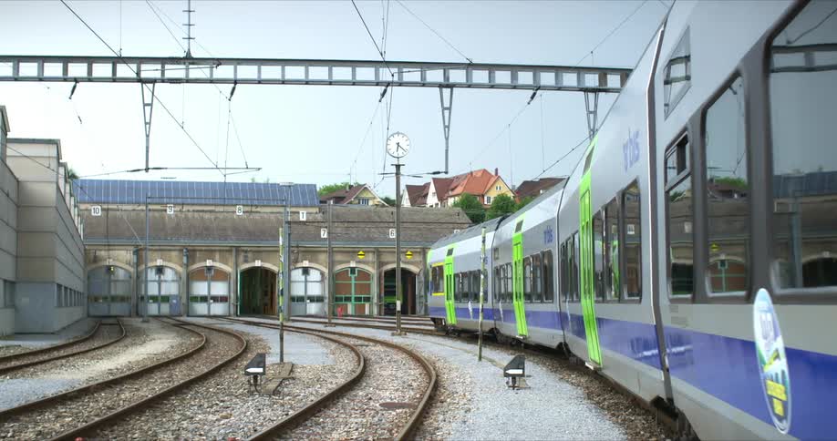 Railway station with a modern train in green and silver tones in motion