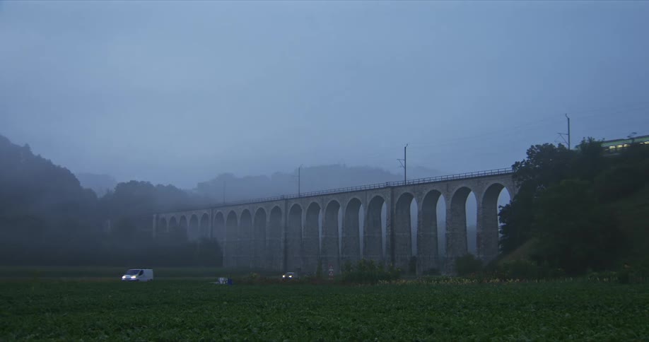 A long arched stone viaduct stretches across a misty green landscape with trees and hills in the background