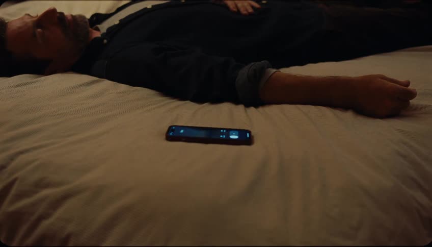 A person sleeping in a bed next to a cell phone with the screen on