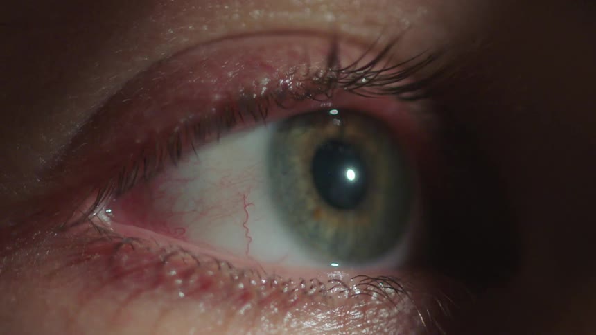 Green eye on a female person blinding with a light reflection on the pupil