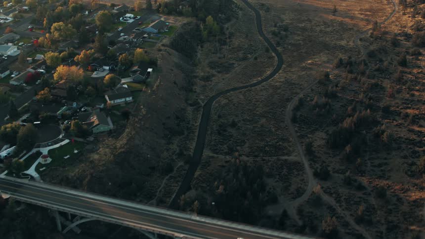 An aerial view of a bridge spanning a dry winding riverbed connecting two residential areas