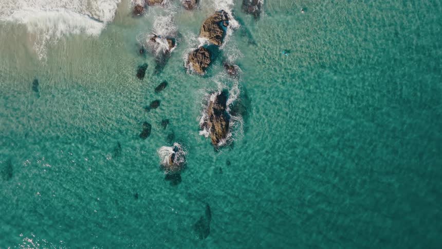An aerial view of a rocky coastline with waves crashing against the shore