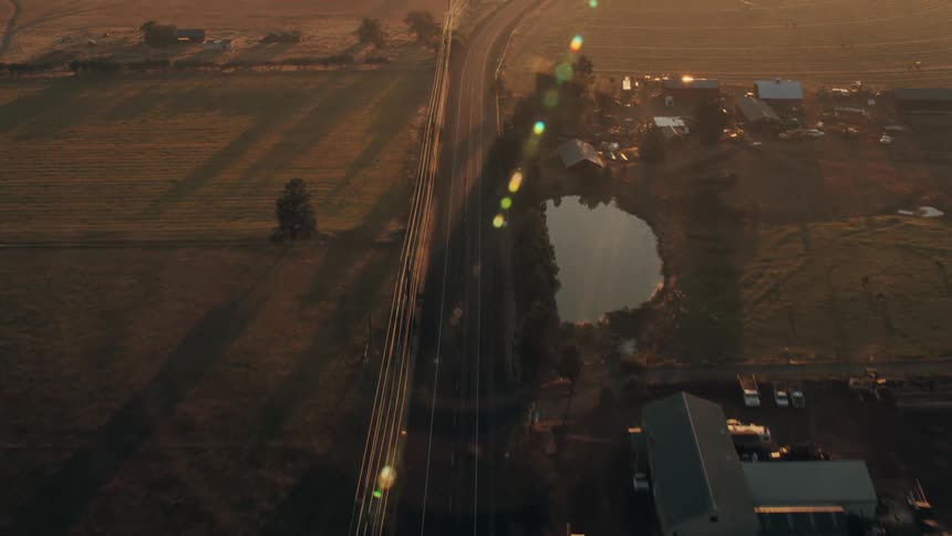 Highway passes through rural farmland while the sun shines over the mountains