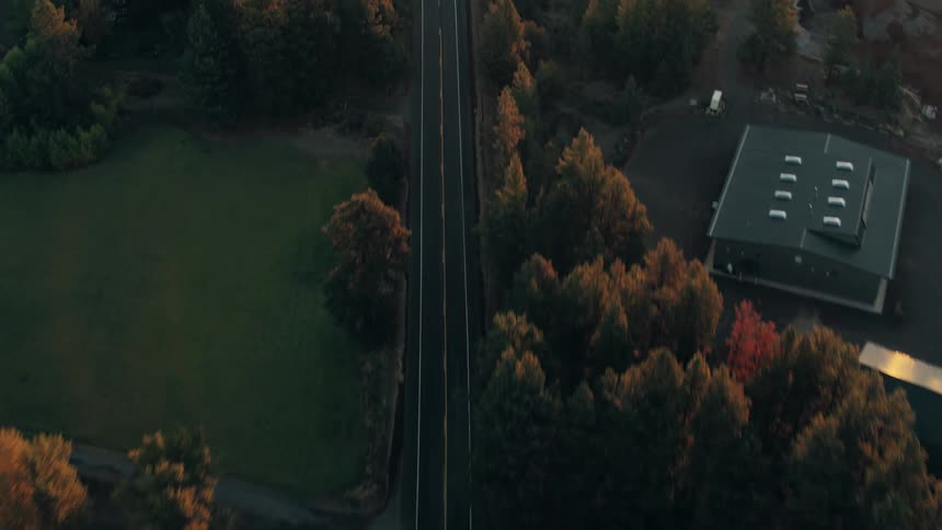 Aerial of a few cars driving along a highway in a rural town on an autumn evening