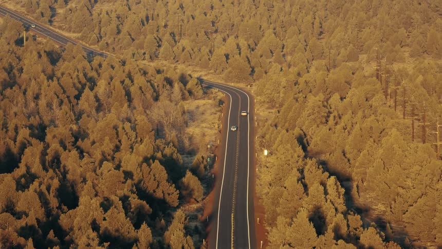 Aerial of vehicles moving along a highway roughly paralleling power lines through a forest