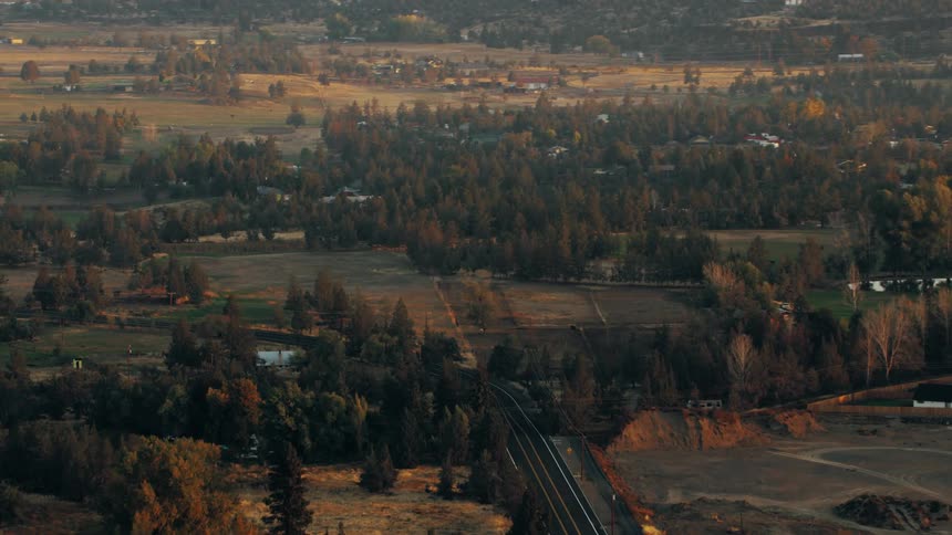 A rural landscape at sunset with fields houses and a road winding through the scene
