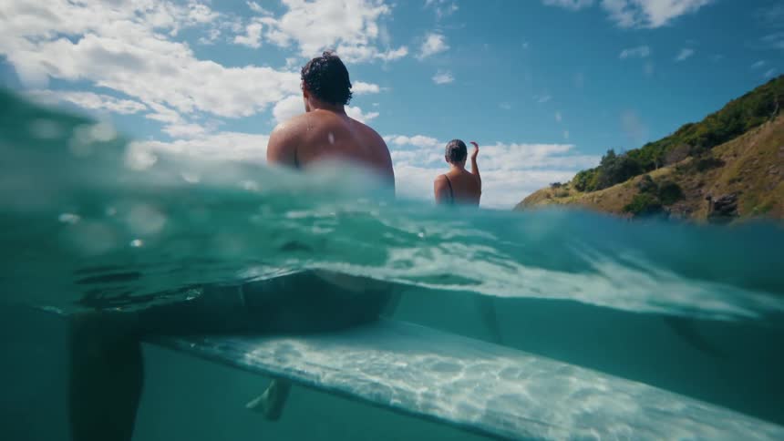 Two people sit on their surfboards in the ocean