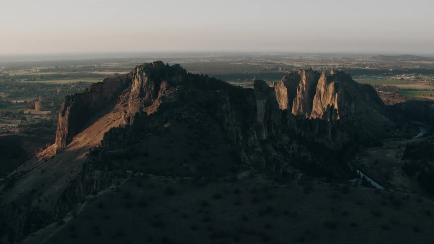 An aerial view of two huge stone mountains in a rural area with grass fields on a small river