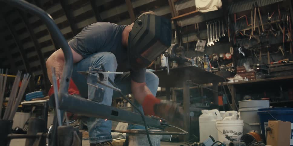 The man in the blue shirt and jeans is wielding a piece of metal then raises his face shield