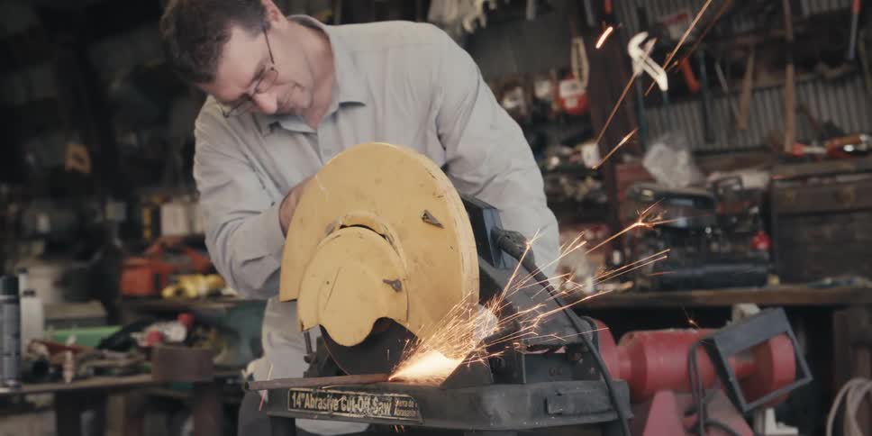 A man cuts a piece of wood with a table saw in a room full of tools