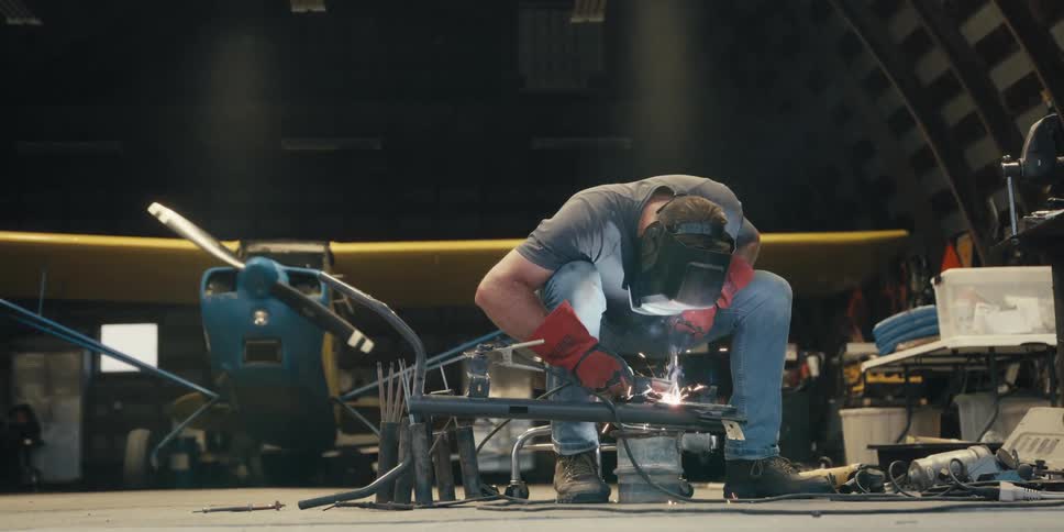 A person in protective gear is welding metal pieces together with bright sparks flying