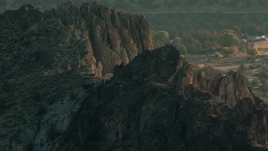 A rugged rocky mountainside rises dramatically against a hazy sky overlooking a vast valley below