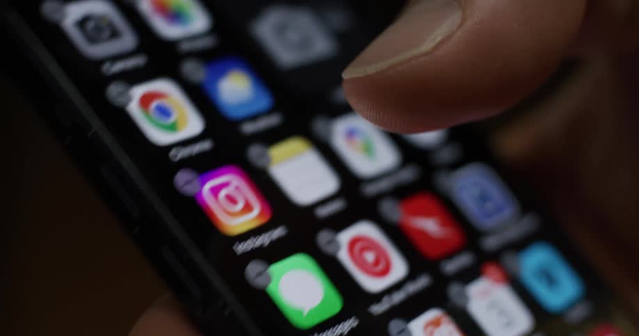 A finger presses the instagram icon on a smartphone screen initiating the process of deleting the app