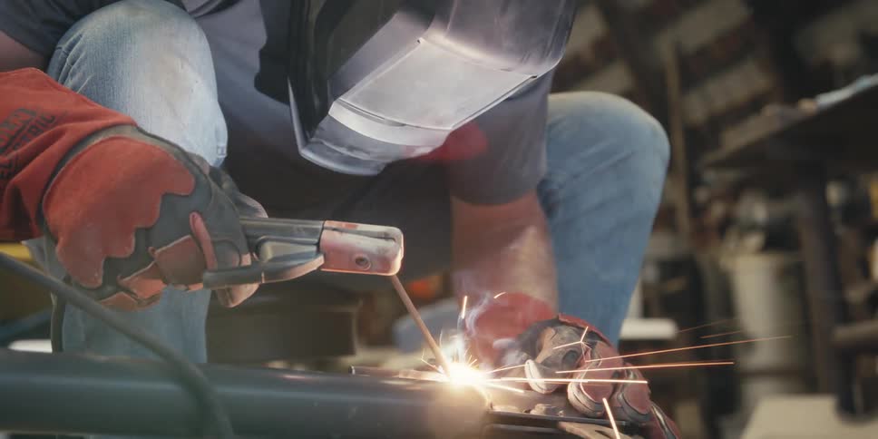 Person in protective helmet holding a tool and welding a metal emitting sparks