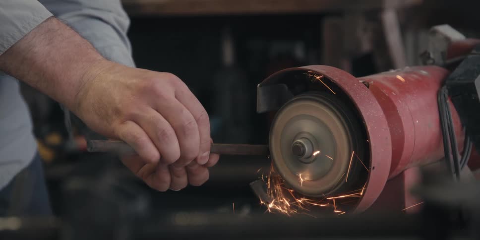Sparks fly as a man smooths the outside of a metal pipe using a machine
