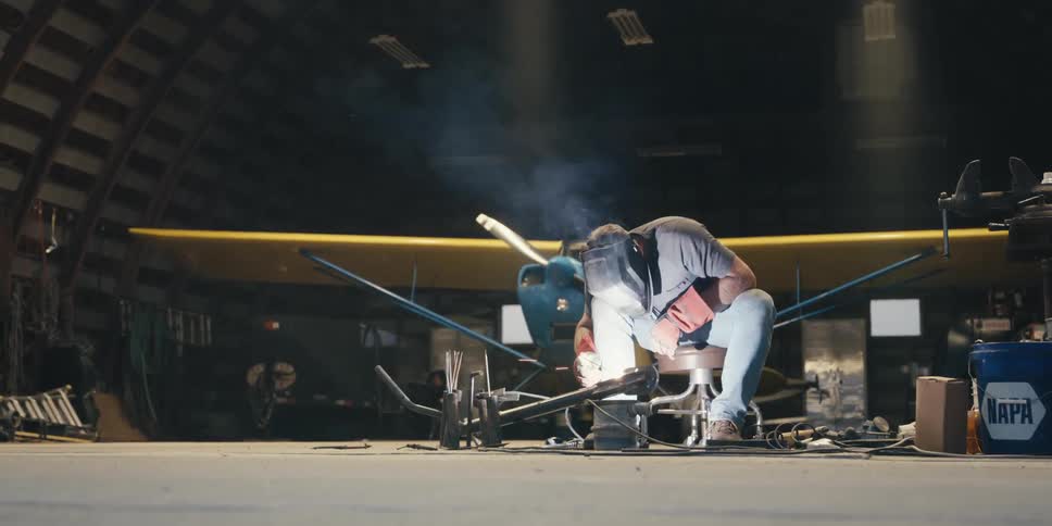 A person wearing red protective gloves is using a power tool to grind a metal pipe producing bright sparks in a workshop setting
