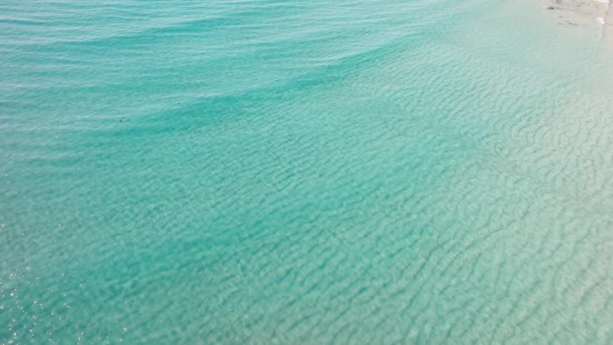 The crystal clear water of a shallow sea shimmers with turquoise hues as gentle waves ripple across its surface