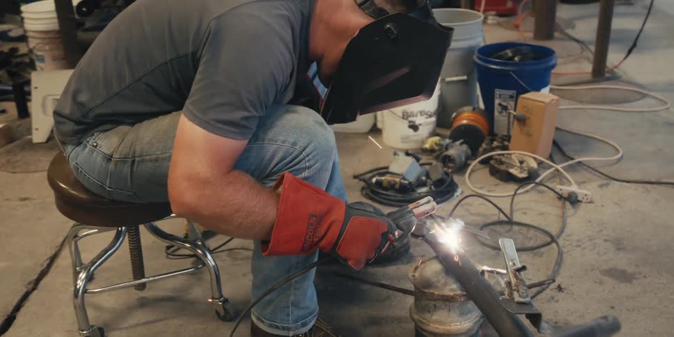A mean leans down welding a pipe