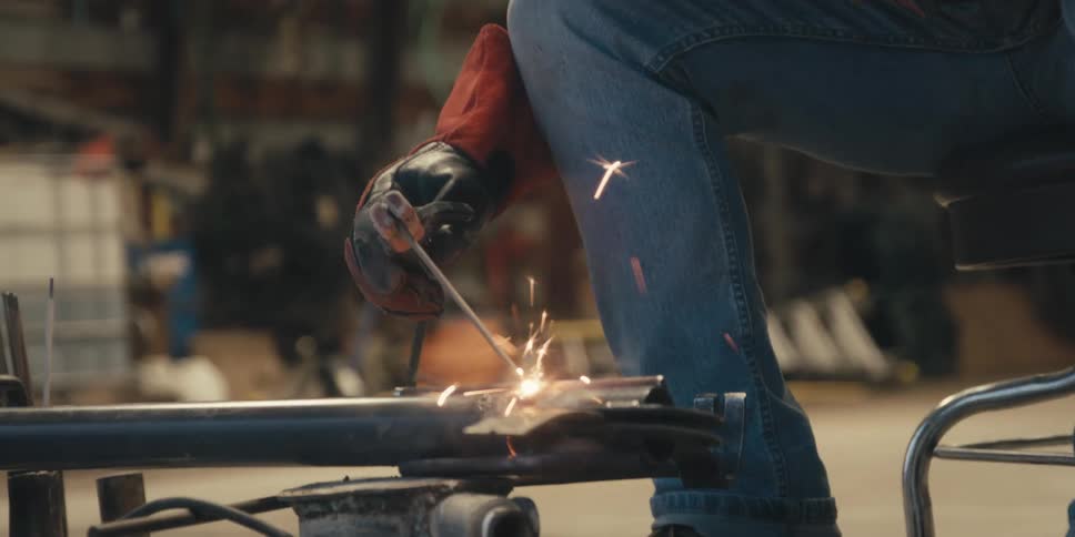 A person in protective gear is welding metal pieces together with bright sparks flying