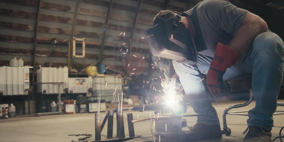 A person in protective gear is welding metal pieces together with bright sparks flying
