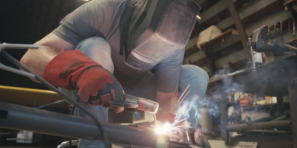 A person in protective gear is welding metal pieces together with bright sparks flying