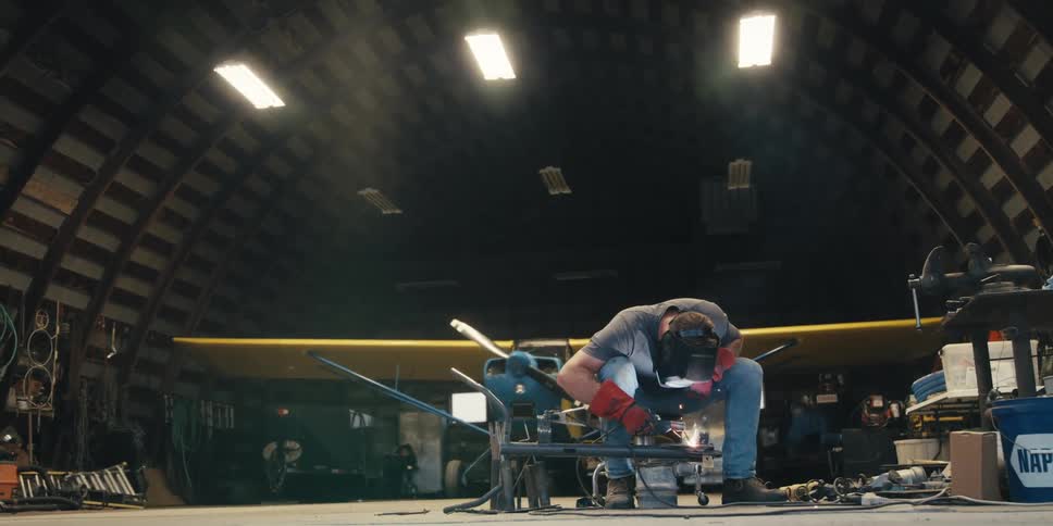 A man wearing a helmet is welding a metal material by releasing several baits in an environment with a circular ceiling