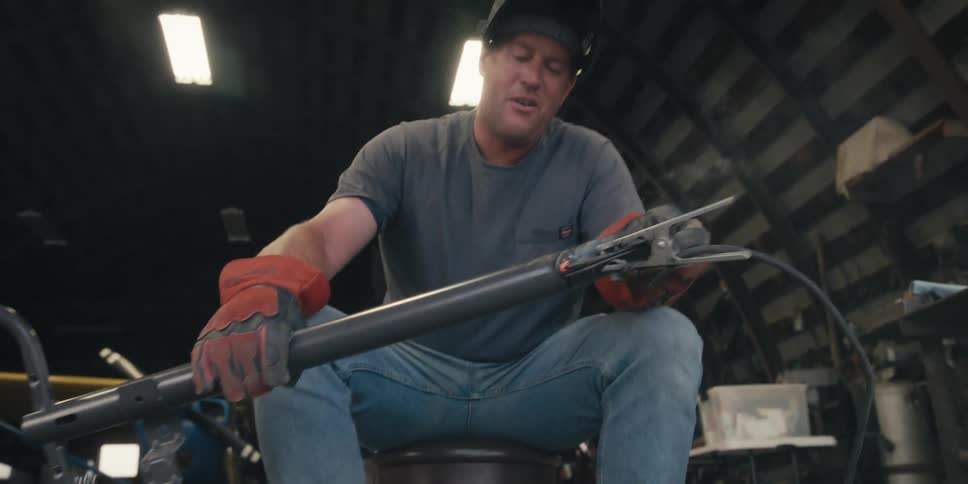 A person in protective gear is holding a metal piece after welding it